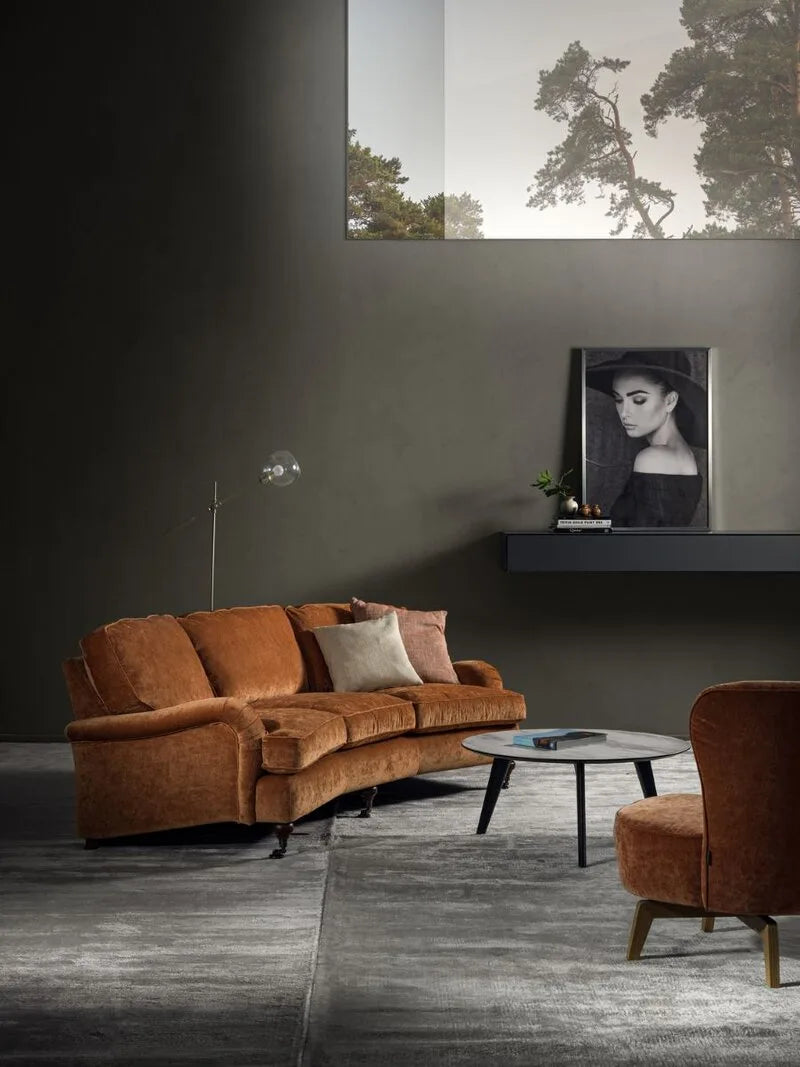 Furninova Sofa in cognacfarbenem Samt mit Sessel, rundem Marmortisch und Stehlampe vor dunkelgrüner Wand.