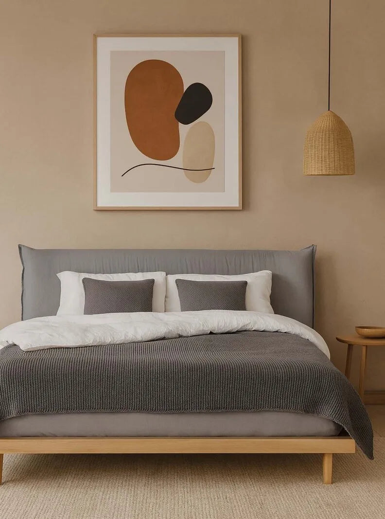 Modernes Schlafzimmer mit grauem Polsterbett aus Holz, weißer Bettwäsche, abstraktem Wandbild, Rattan-Pendelleuchte und warmen Beigetönen.