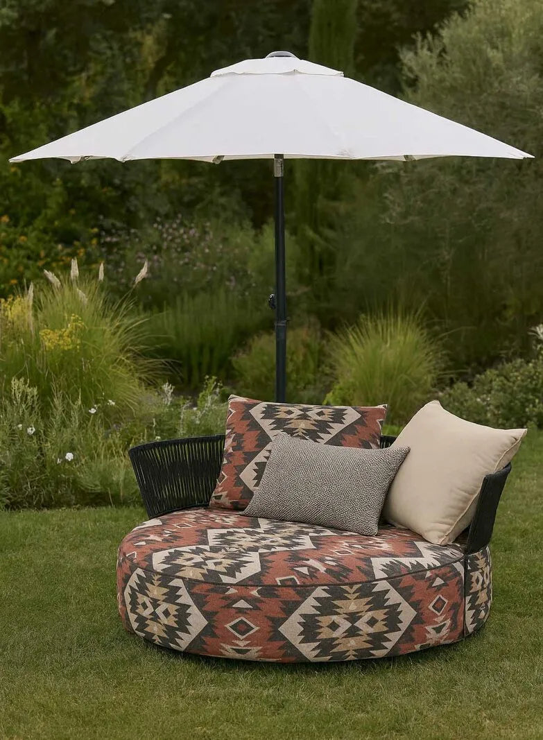 Bullfrog Outdoor-Loungesessel mit gemustertem Bezug in Terrakotta und Schwarz, beigem Kissen und cremefarbenem Sonnenschirm im Garten.