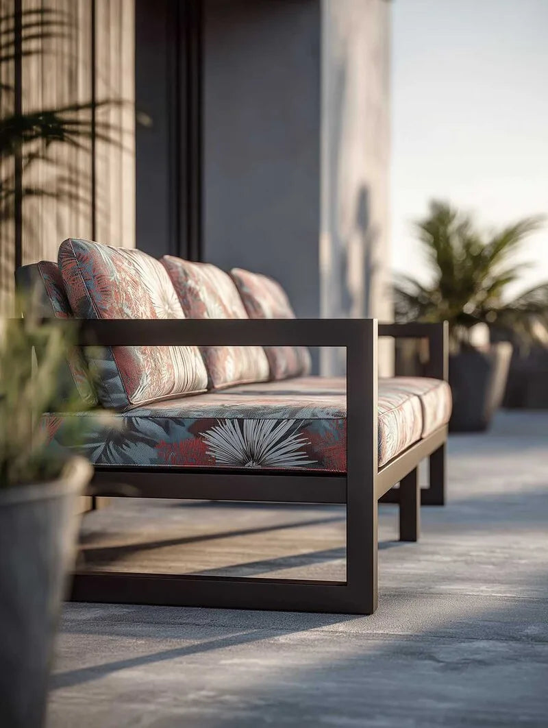 Modernes Outdoor-Sofa mit schwarzem Aluminiumrahmen und floral gemusterten Polstern in Rot- und Blautönen auf sonniger Terrasse.